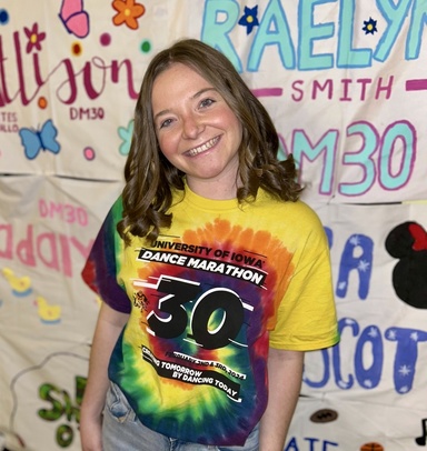 woman standing in front of a drawn-on background and wearing a dance marathon shirt