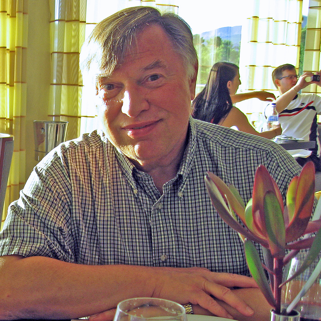 man with grey hair and blue button down shirt sitting in front of table