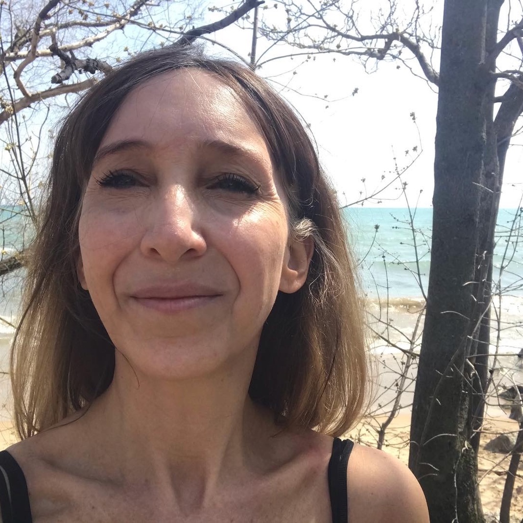 headshot of a woman in front of a stand of trees and some water 