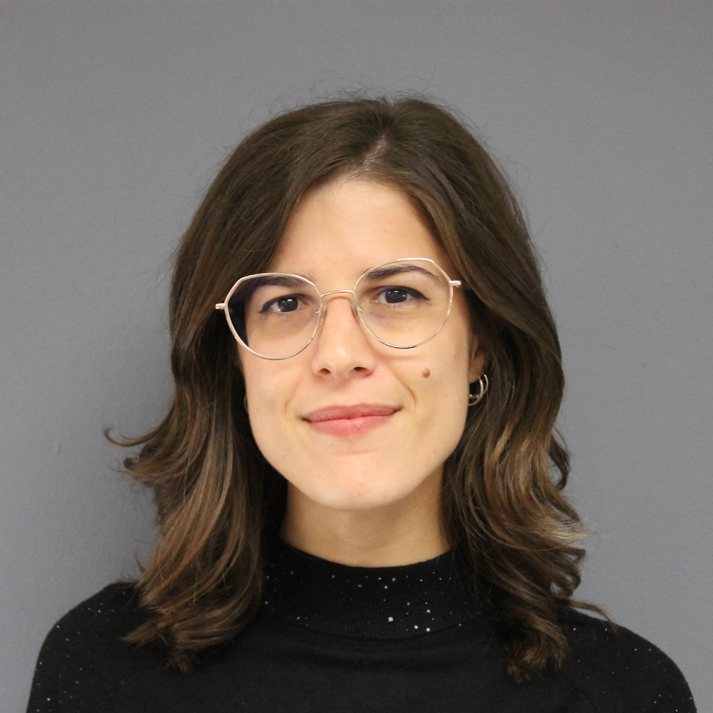 young woman with shoulder length brown hair, wearing glasses, slight smile
