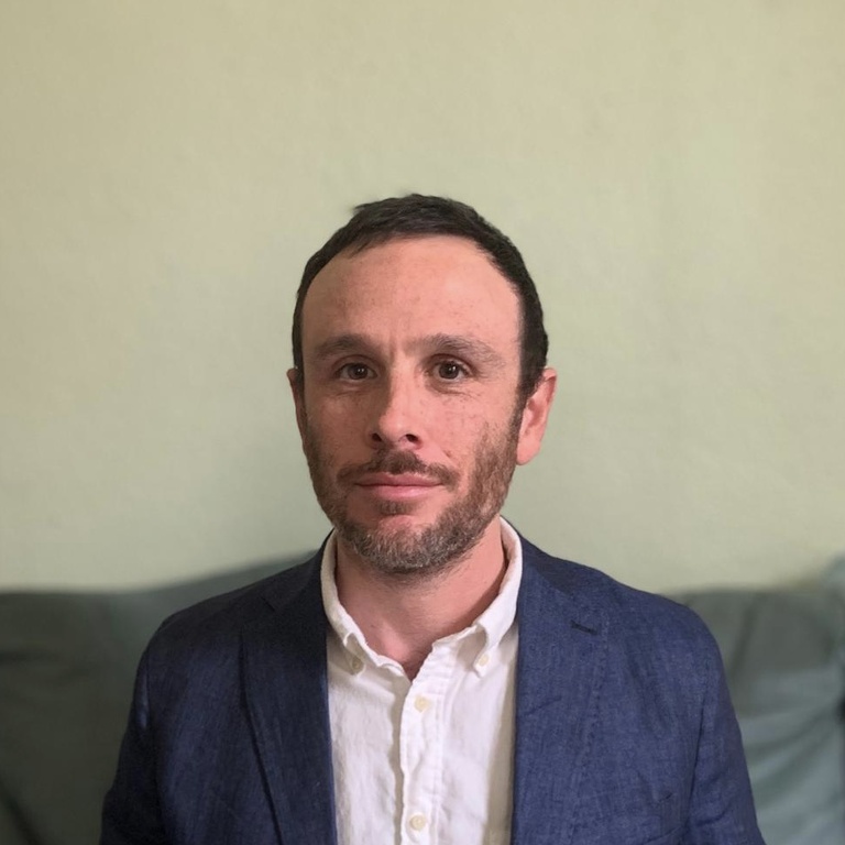Photo from torso up of man with short hair and short beard wearing suit