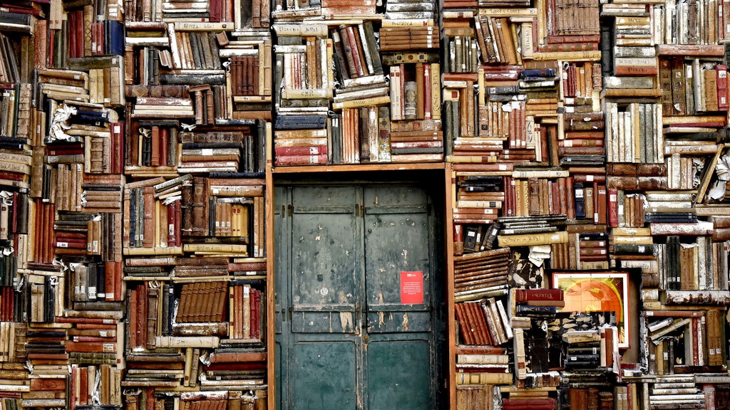 A green door peeking through stacks and stacks of books.